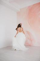 Young bride in white dress with flower wreath on her head dancing in the studio photo