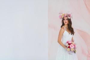 Young bride in white dress with flower wreath on her head posing in the studio photo