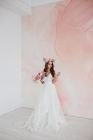 Young bride in white dress with flower wreath on her head posing in the studio photo