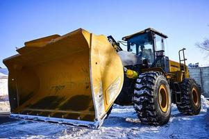 retroexcavadora cargador en el la carretera. un amarillo tractor elimina nieve en el calle. foto