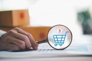 Startup or small business entrepreneur holding a magnifying glass, and the shopping cart icon and ordering order, Internet shopping, online shopping on the Internet, SME, shipping boxes, e-commerce photo
