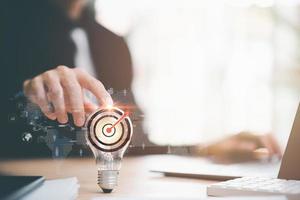 businessman pointing to a light bulb and arrow icon hitting center of dartboard target,Setting business goals and focused concepts, Organizational growth and objectives, marketing strategy planning photo