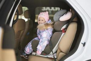 Child safety seat chair with baby girl is on back seat of car. photo