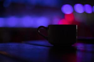 Cup on table in bar. Coffee mug in restaurant. Drink cup in purple light. Interior details. photo