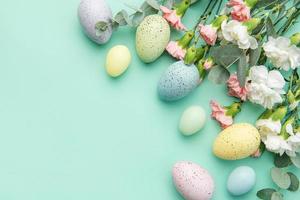 Easter colored eggs and a bouquet of white and pink carnations with eucalyptus branches on a soft green background. photo