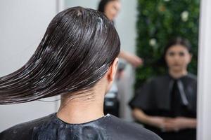 Hairdresser applies a hair mask to straight black hair. Hair care at the beauty salon. photo