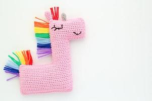 Crochet amigurumi handmade stuffed soft pink unicorn toy with rainbow mane on white background. Handwork, hobby. Craft diy newborn pregnancy concept. Knitted doll for little baby. Close up flat lay photo