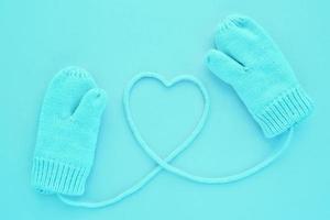 Close-up blue mittens and heart symbol shaped of string on blue background. Lifestyle and warm feelings concept. Valentine day. Monocolor romantic pattern. Winter theme. Flat lay composition. Top view photo