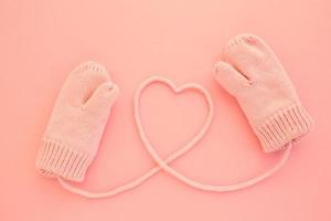 Close-up pink mittens and a heart symbol shaped of string on pink background. Lifestyle and warm feelings concept. Valentine day. Monocolor romantic pattern. Flat lay composition. Top view photo