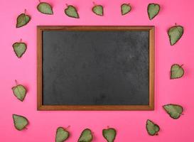empty wooden frame on a pink background, decorating with green fresh leaves photo