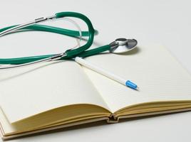 open blank notebook with pen and stethoscope, white table photo