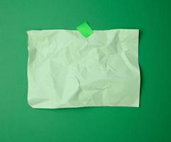 rectangular crumpled blank green sheet of paper glued with green sticky paper on green background photo