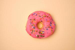 pink round donut with colored sprinkles on a beige background photo