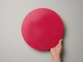 female hand holds empty red plastic textured cake plate on a gray background, top view photo