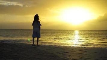 adorabile contento poco ragazza su bianca spiaggia a tramonto. video