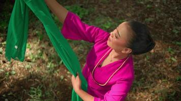 Javanese woman holding the green scarf while the wind moves the scarf in the air inside the jungle video