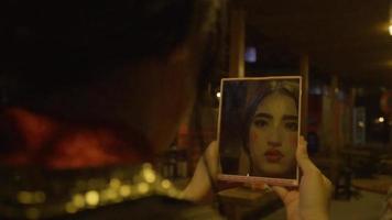 A Chinese Woman holding a mirror while looking at her face with clown makeup video