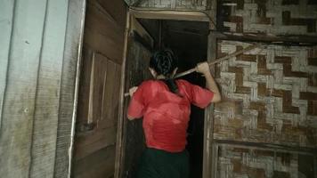 blind kvinna gående genom de dörr med de pinne medan bär en röd skjorta inuti de fattig hus video