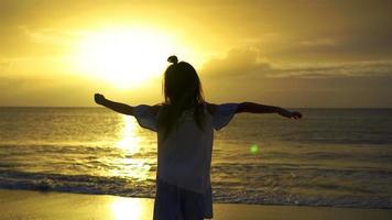 Adorable happy little girl on white beach at sunset. Silhouette of little girl on the coast on a beautiful sunset video