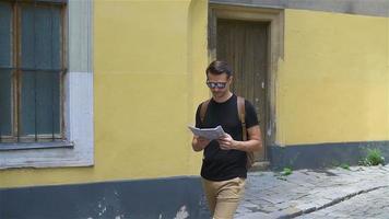 mann tourist mit stadtplan und rucksack in der europastraße. kaukasischer junge, der mit karte der europäischen stadt schaut. video