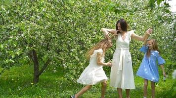 adorable pequeño muchachas con joven madre en floreciente jardín en hermosa primavera día teniendo divertido juntos video