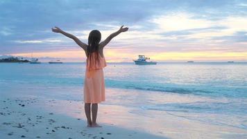 bezaubernd glücklich wenig Mädchen Gehen auf Weiß Strand beim Sonnenuntergang. schleppend Bewegung video