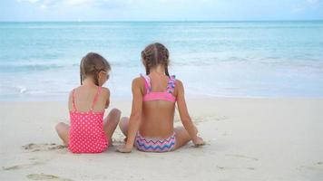 schattige kleine meisjes spelen met zand op het strand. kinderen zitten in ondiep water en maken een zandkasteel