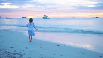 Adorable happy little girl on white beach at sunset. video