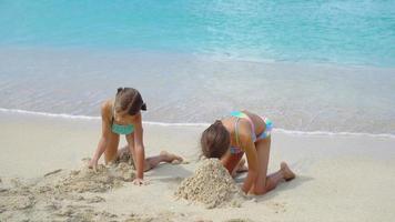 Two little happy girls have a lot of fun at tropical beach playing together at shallow water. Kids splashing.