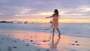 adorabile contento poco ragazza su bianca spiaggia a tramonto. video