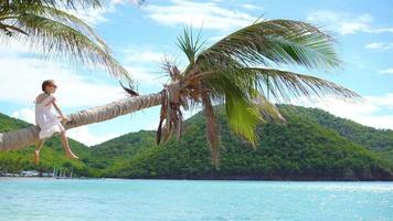 aanbiddelijk weinig meisje Bij tropisch strand zittend Aan palm boom gedurende zomer vakantie video