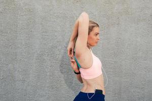 Sportive girl near the wall in headphones stretches muscles photo