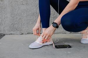 deportivo niña atadura cordones de los zapatos cerca el pared en auriculares foto