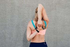 Sportive girl near the wall in headphones stretches muscles photo