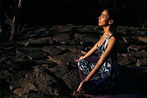 Girl meditates in nature sits with closed eyes on stones photo