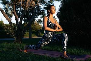 A girl is engaged in yoga in nature on a phylote mat warrior pose watching the sunset photo