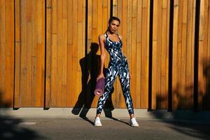 sports girl on a wooden wall background with mats in hand full-length portrait photo