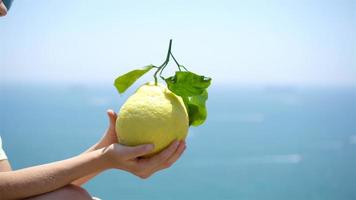 Big yellow lemon in hand in background of mediterranean sea and sky. video