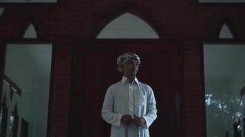 musulmán hombres en pie y Orando en frente de el marrón mezquita durante el Mañana video