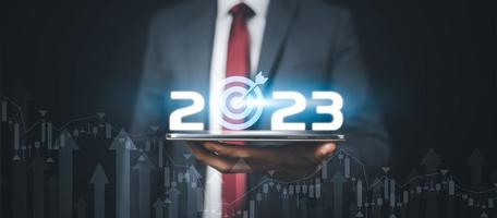 Businessman holds tablets with target and number new year 2023 on the business graph background  Innovative new ideas of inspiration from online technology, Changes in new planning, Business Growth photo