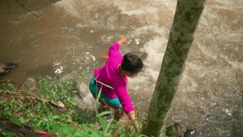 Asian woman walking on the edge of the river while wearing a pink dress and green skirt in makeup with a lot of rock video