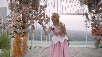 A Princess in a pink dress playing in the cage in the garden while the flowers surrounding her video