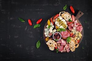 Antipasto platter with ham, prosciutto, salami, blue cheese, mozzarella with pesto and olives on a wooden background. Top view, overhead photo