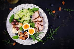 Ketogenic diet. Keto brunch. Boiled egg, pork steak and olives, cucumber, spinach, brie cheese, nuts and blueberry. Top view photo