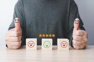 businessman thumbs up on the happy smiling face and five stars icon on the wood block square to give satisfaction in service. rating very impressed.Customer service evaluation and Satisfaction concept photo