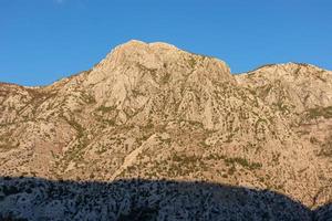 Panoramic view of the steep mountain peaks of Derinski Vrh and Volujak during sunrise seen from the bay of Kotor, Montenegro, Balkas, Europe. First sunbeams on Lovcen  mountains in Dinaric Alps photo
