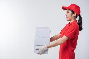 imagen de un joven repartidor con uniforme de camiseta en blanco con gorra roja de pie con una caja de cartón blanca vacía aislada en un estudio de fondo gris claro foto