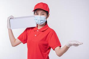 Image of a conscious young delivery man in red cap blank t-shirt uniform face mask gloves standing with empty white cardboard box isolated on light gray background studio photo