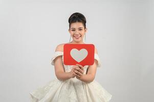 hermosa novia asiática sonriendo y posando con el signo del corazón en el fondo blanco foto