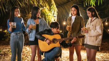 Portrait of Happy Asian group of friends having fun to music dining and drinking together outdoor - Happy friends group toasting beers  - People, food, drink lifestyle, new year celebration concept. photo